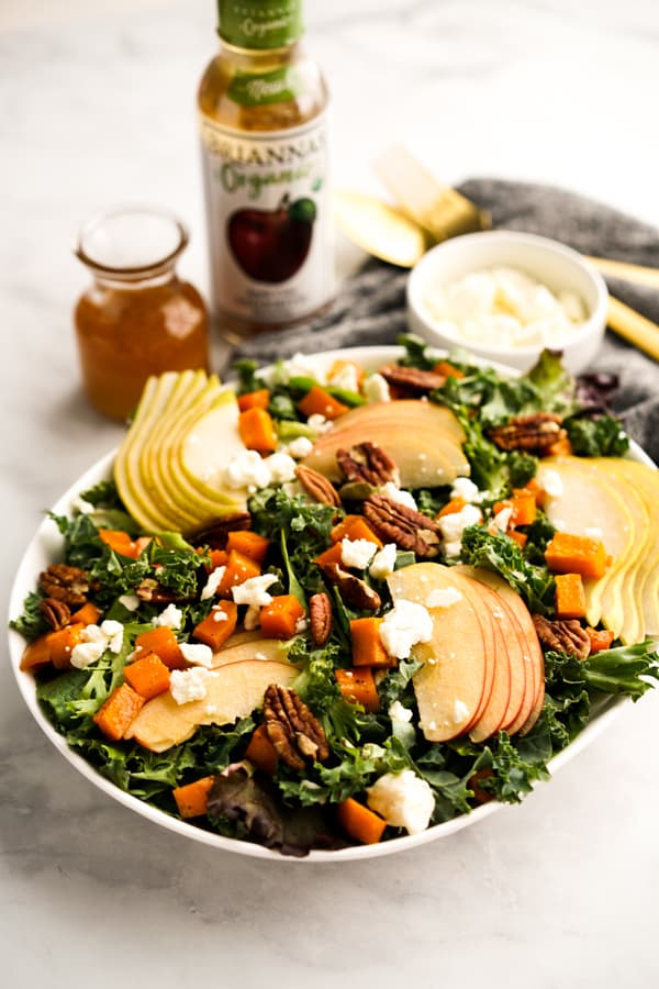 A plate of Fall themed salad with vinaigrette behind it