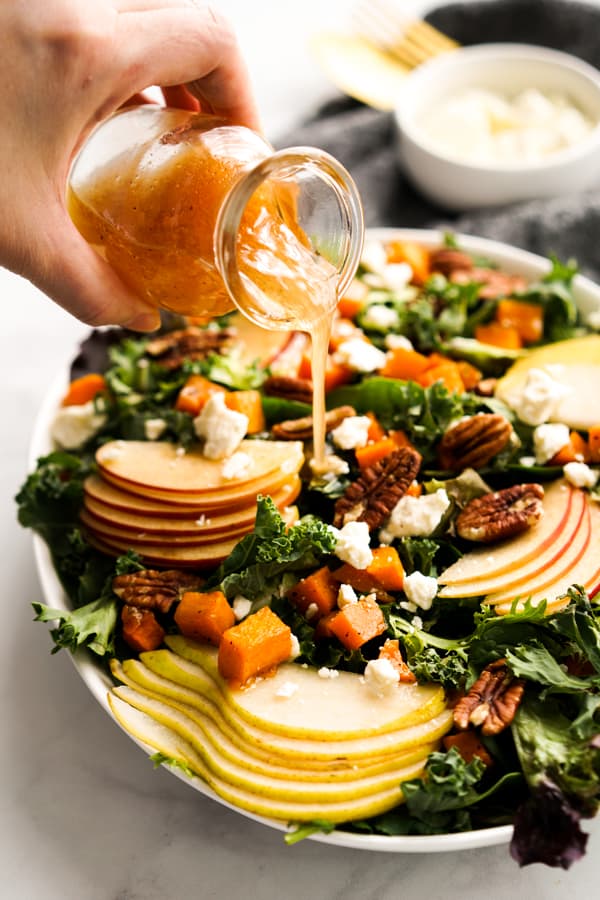 Pouring apple cider vinaigrette onto a salad topped with Fall ingredients