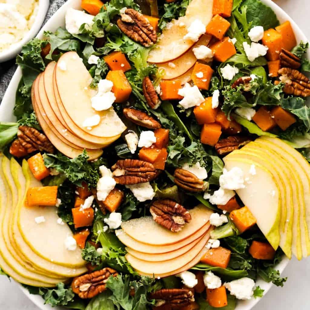 A bowl of kale and green topped with sliced apples, pears, butternut squash, and feta