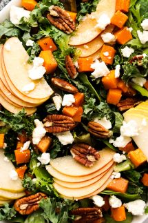 A bowl of kale and green topped with sliced apples, pears, butternut squash, and feta