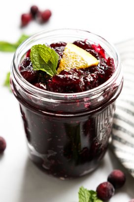A jar of homemade cranberry sauce with mint leave and orange wedge on top