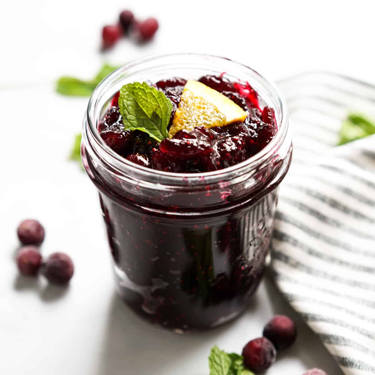 A jar of homemade cranberry sauce with mint leave and orange wedge on top