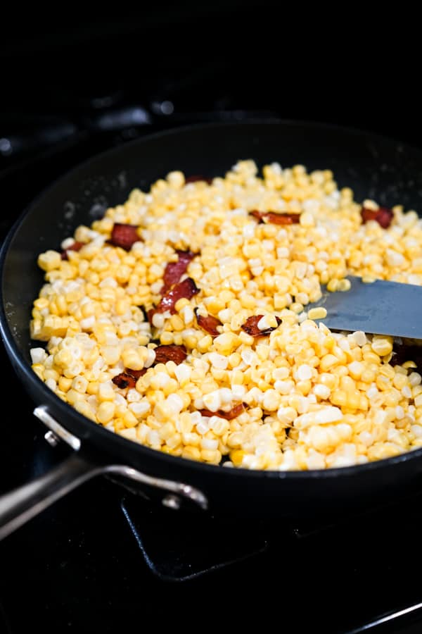 Uncooked corn kernels and bacon in a skillet