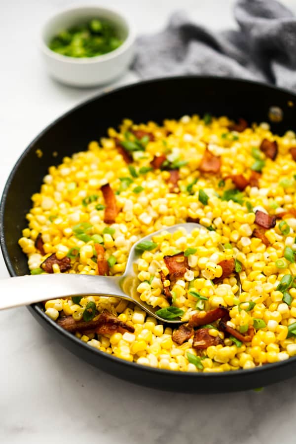 A spoon digging into corn in a skillet