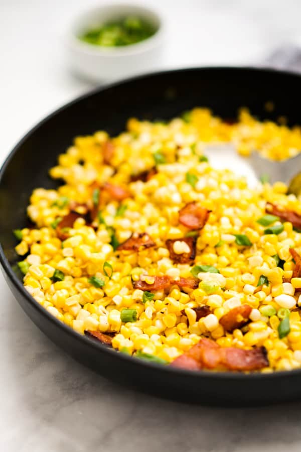 Closeup of pan fried corn in a skillet, with bacon pieces and green onions on top