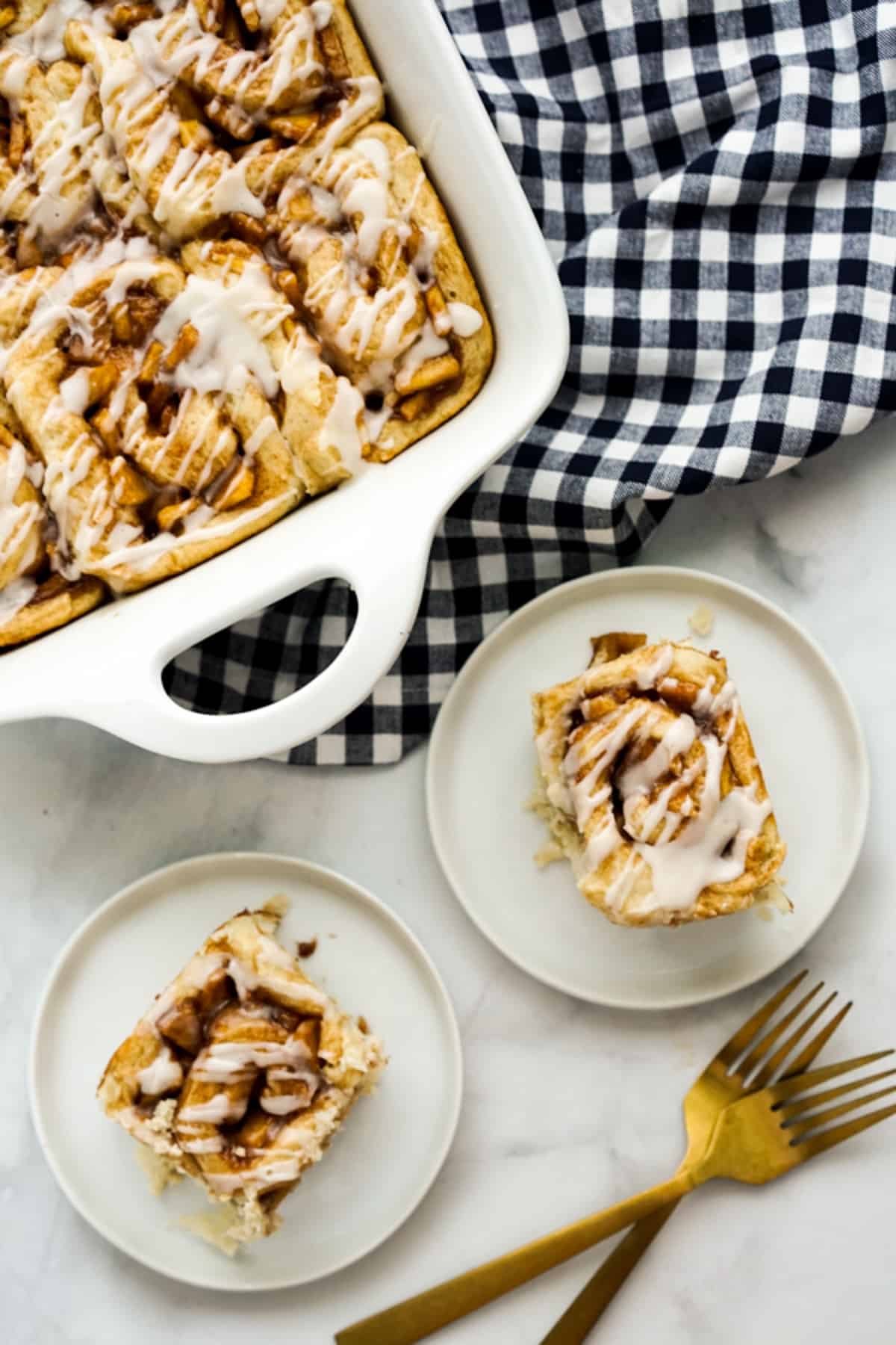 A casserole dish of cinnamon rolls and two plates of cinnamon rolls