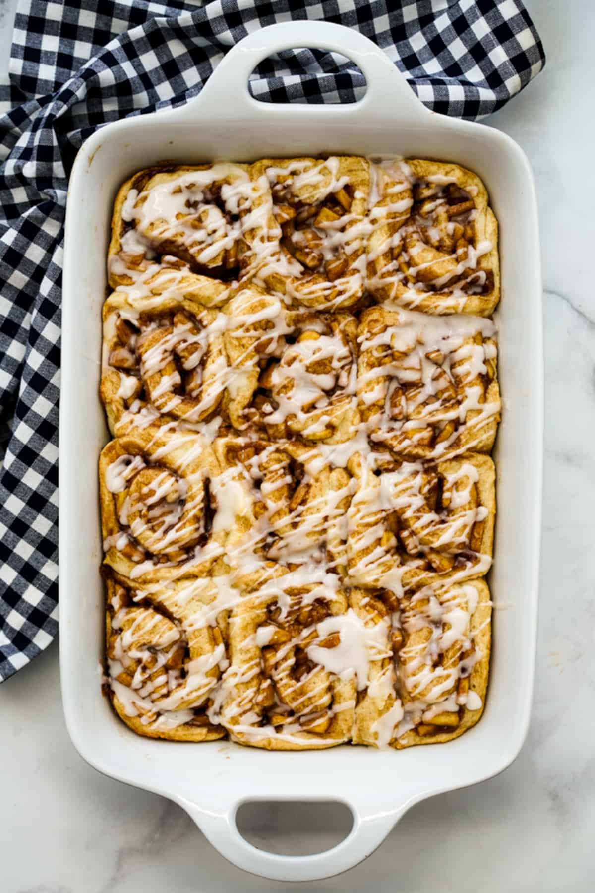A rectangular casserole of cinnamon rolls filled with apple pie filling and drizzled with sweet glaze