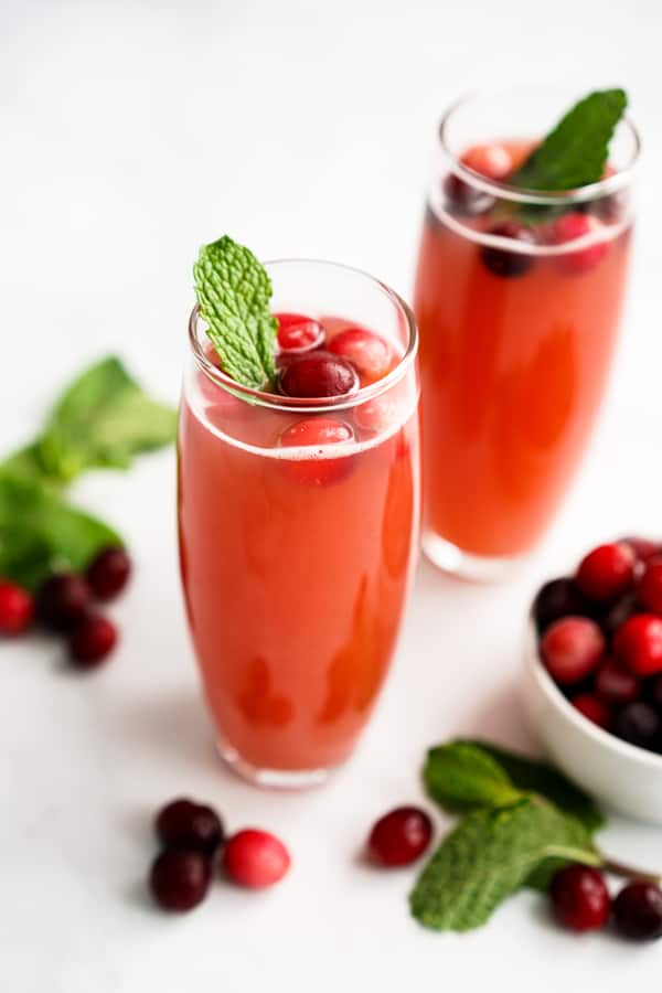 Two glasses of cranberry mimosa in champagne flutes topped with cranberries and fresh mint leaves