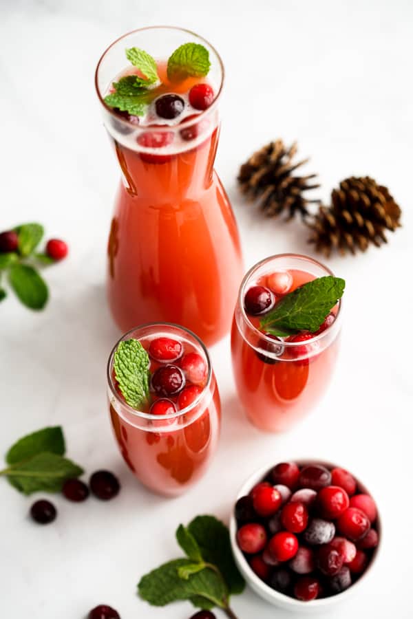 A just and two individual glasses of champagne flutes filled with a bright red drink