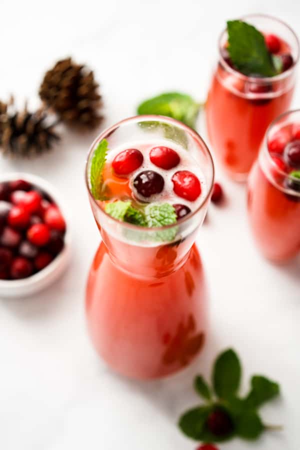 A tall jug filled with red sparkling beverage topped with cranberries and mint leaves