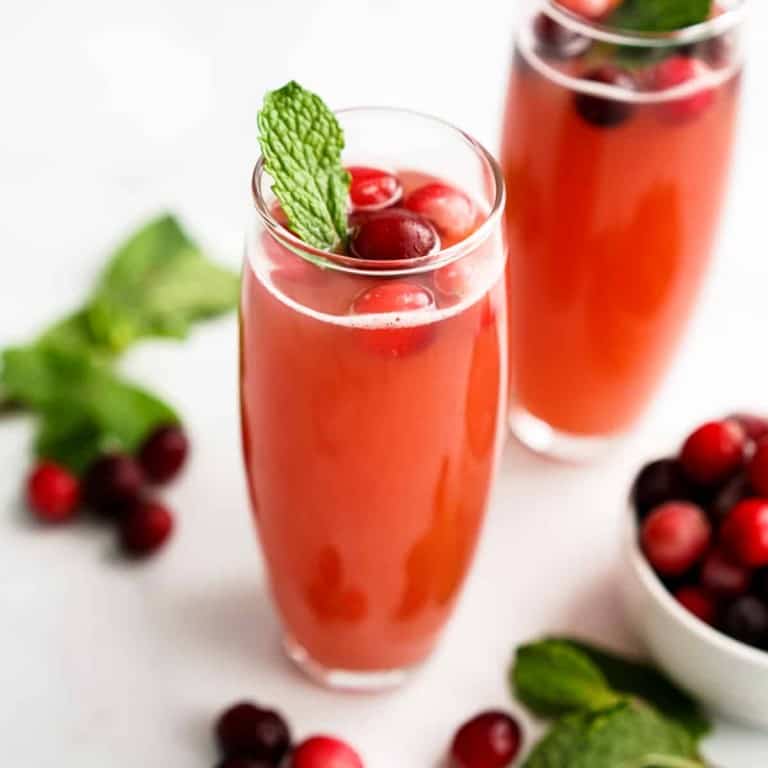 Cranberry mimosa in champagne flute with mint leaves and cranberries