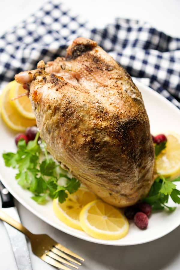 A whole turkey breast on a platter with herbs, lemons and cranberries around it