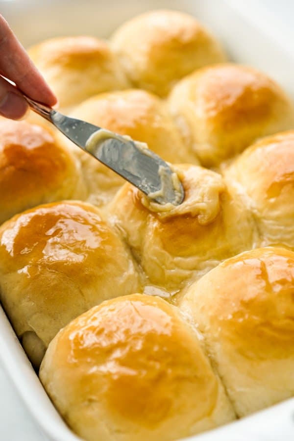 Spreading Honey Butter onto a casserole of dinner rolls