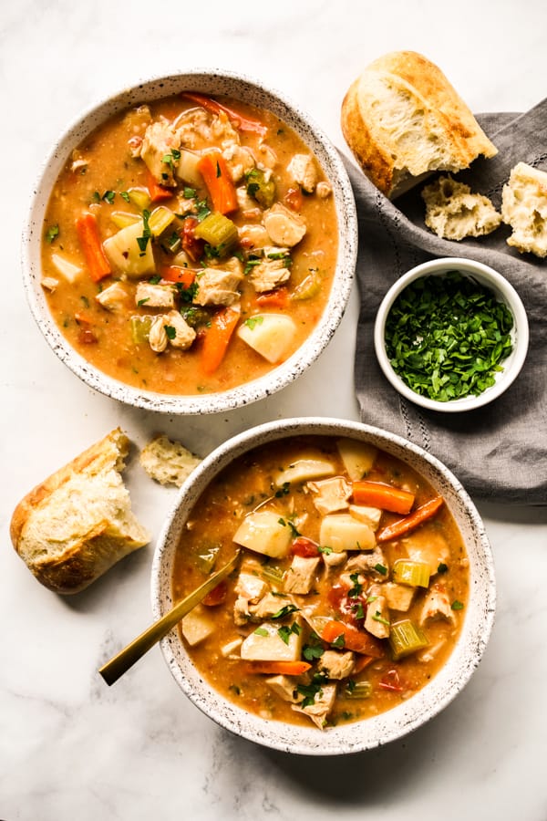 Two bowls of turkey stew from top down, along with crusty bread