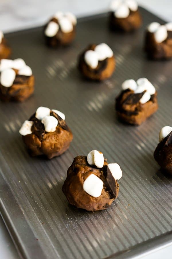 Round raw chocolate cookie dough on baking sheet topped with mini marshmallows