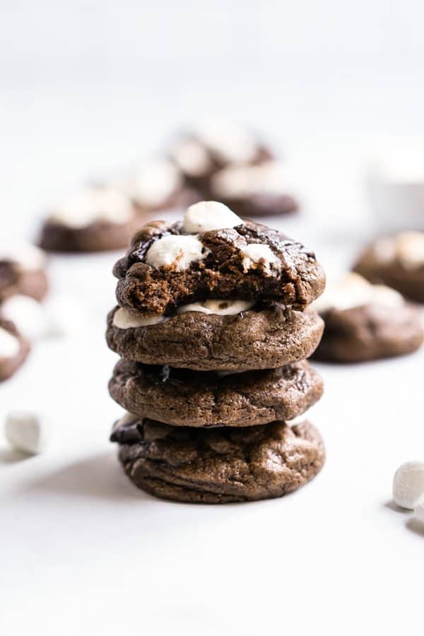 A stack of thick chocolate cookies with marshmallows on top, the top cookie is half eaten