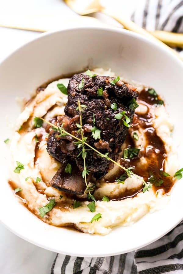 Braised short ribs sitting on top of a bed of mashed potatoes, smothered with gravy
