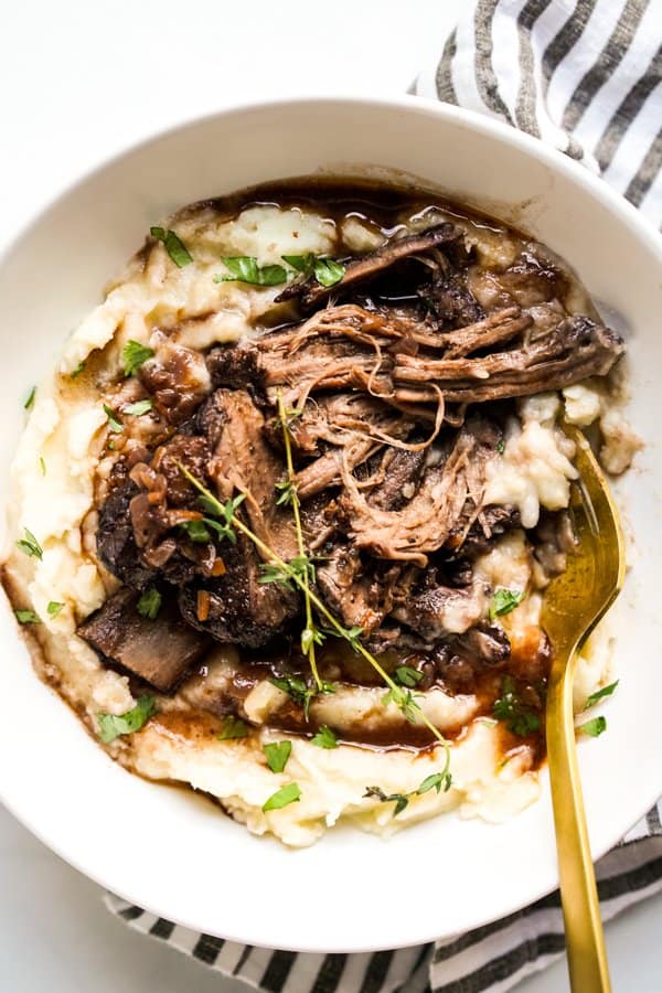 Fall apart short ribs on top of mashed potatoes in a bowl, with fork next to it