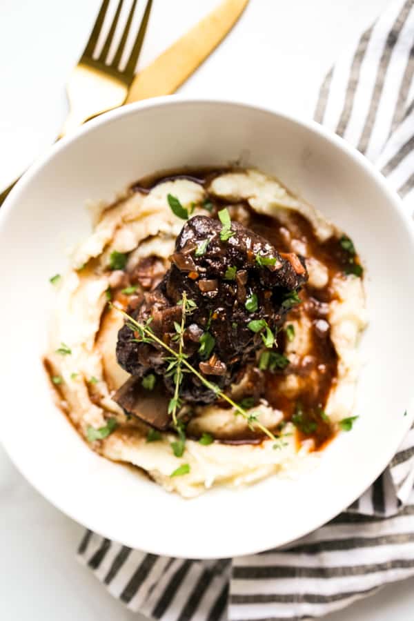 A plate of mashed potatoes topped with Red Wine Braised Short Ribs and gravy