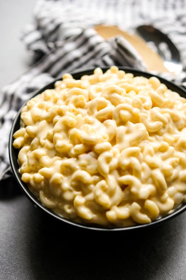 A bowl of creamy mac and cheese with kitchen towel and spatulas in the background