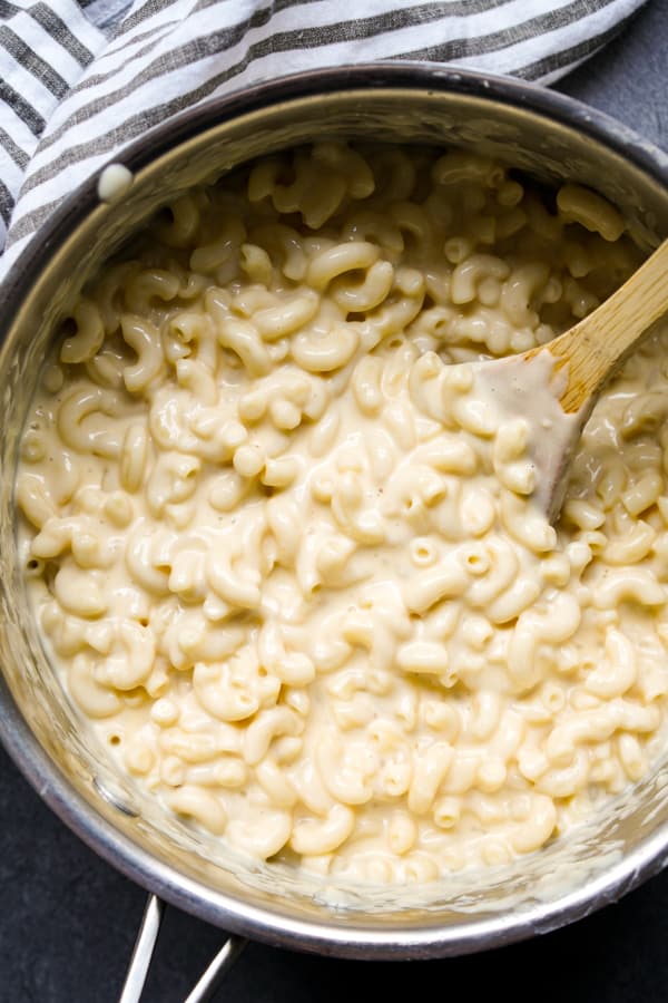 Top down view of macaroni and cheese in a pot, stirred with a wooden spatula