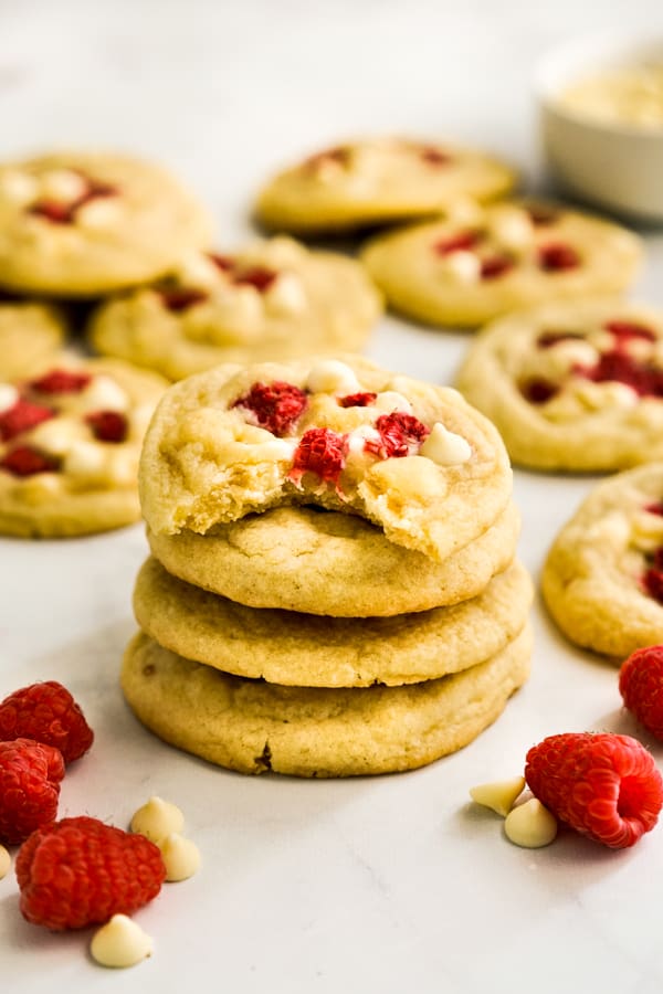 A stack of White Chocolate Raspberry Cookies with raspberries and more cookies around the stack 