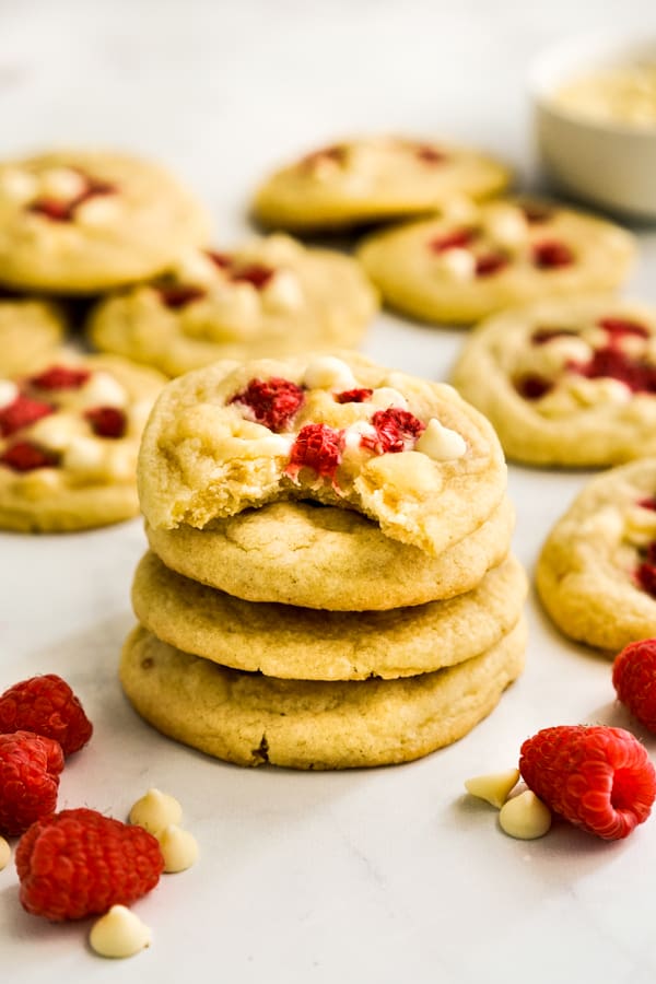 A stack of White Chocolate Raspberry Cookies with raspberries and more cookies around the stack