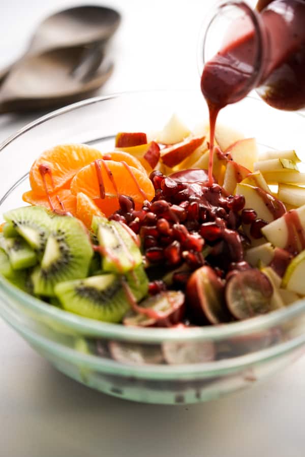 Pouring raspberry poppyseed dressing onto a bowl of fruits