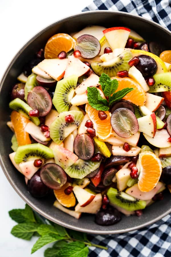 A bowl of fruit salad with mandarin oranges, pear, apple, grapes kiwi and pomegranate