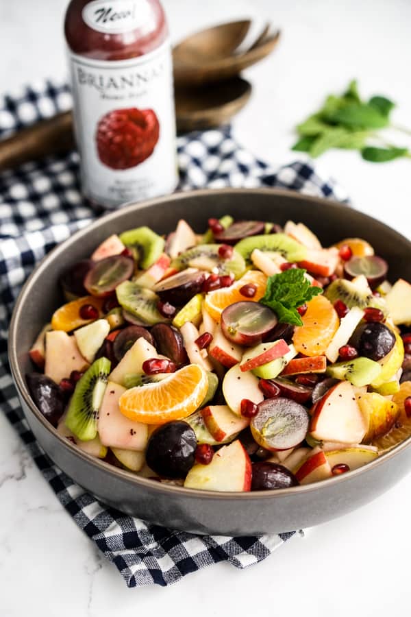 A bowl of fruit salad with a bottle of dressing in the background