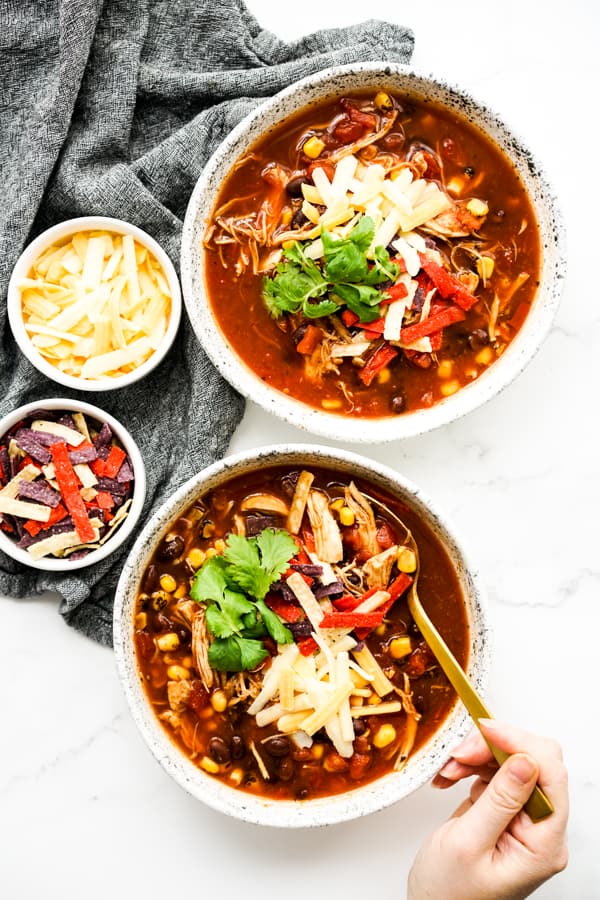 Two bowls of chicken taco soup garnished with cheese, cilantro and tortilla strips