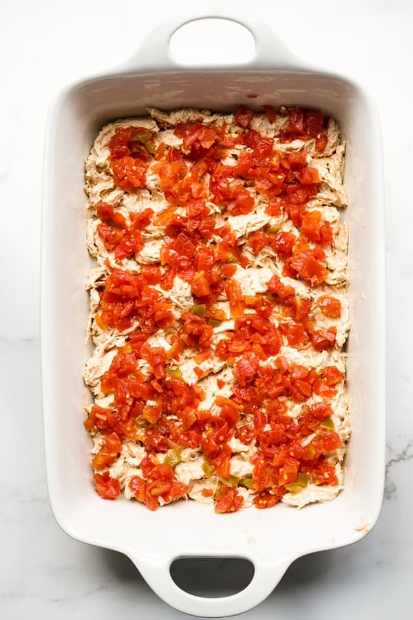 tomatoes and green chilies on top of shredded chicken in a rectangular casserole dish