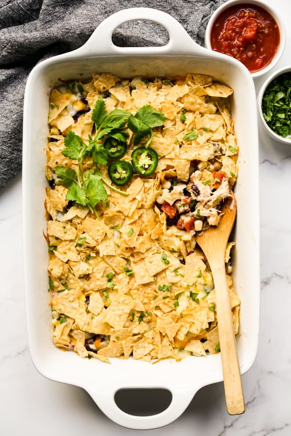 A wooden spoon digging into a rectangular dish of Mexican Chicken Casserole, salsa on the side