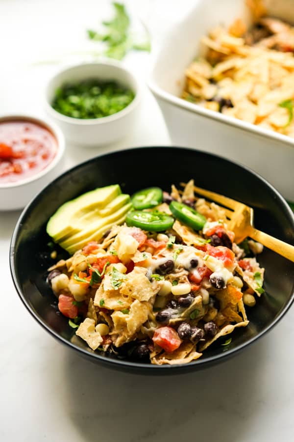 A bowl of Chicken Mexican Casserole garnished with avocado and jalapeño, with the casserole dish in the background