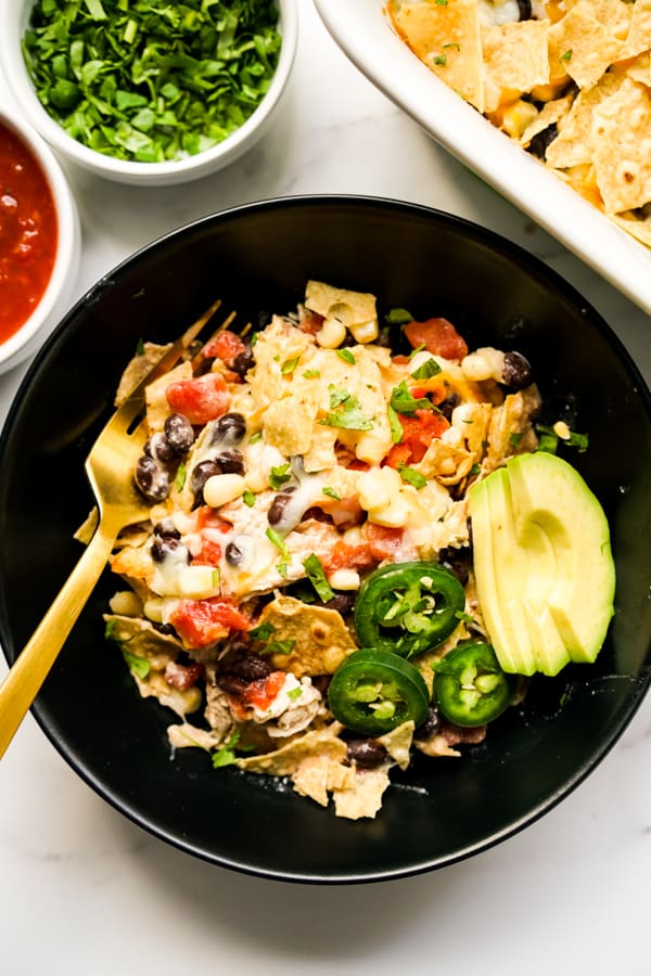 A black bowl with a serving of Mexican Chicken Casserole topped with cilantro, avocados and jalapeño 