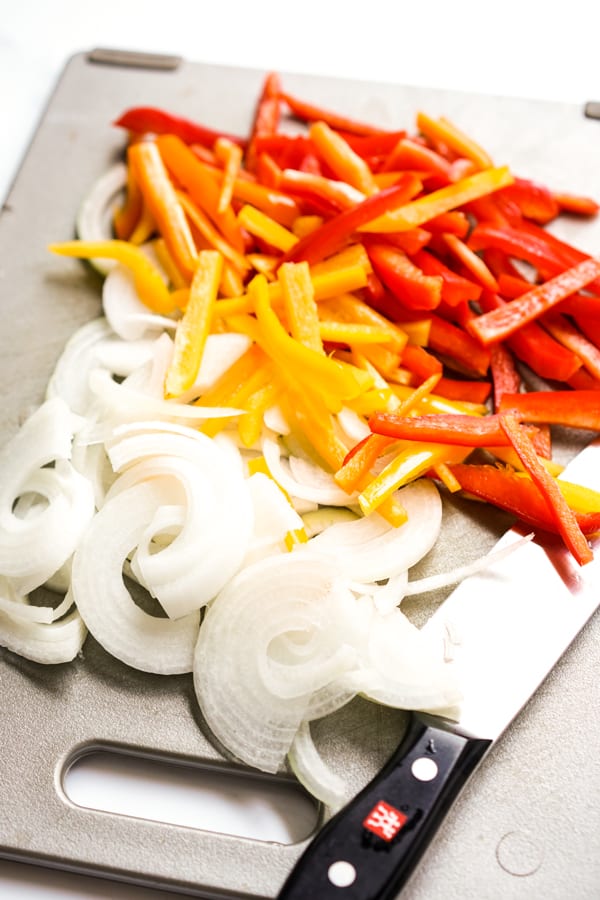 orange and red bell peppers along with onions on a cutting board