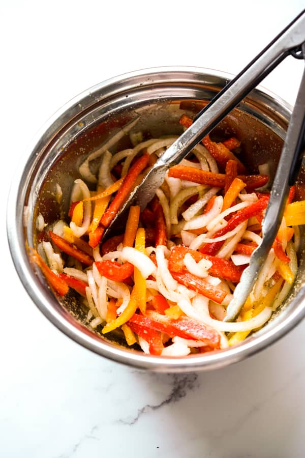 A bowl of sliced bell peppers and onions in a mixing bowl