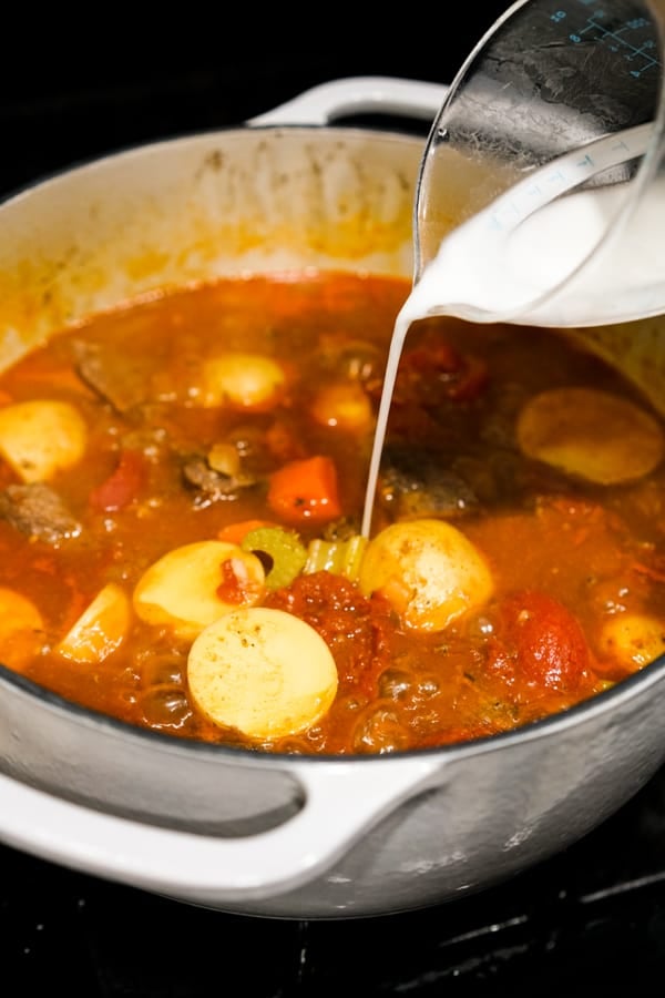 Pouring cornstarch mixture into pot on the stovetop to thicken beef stew