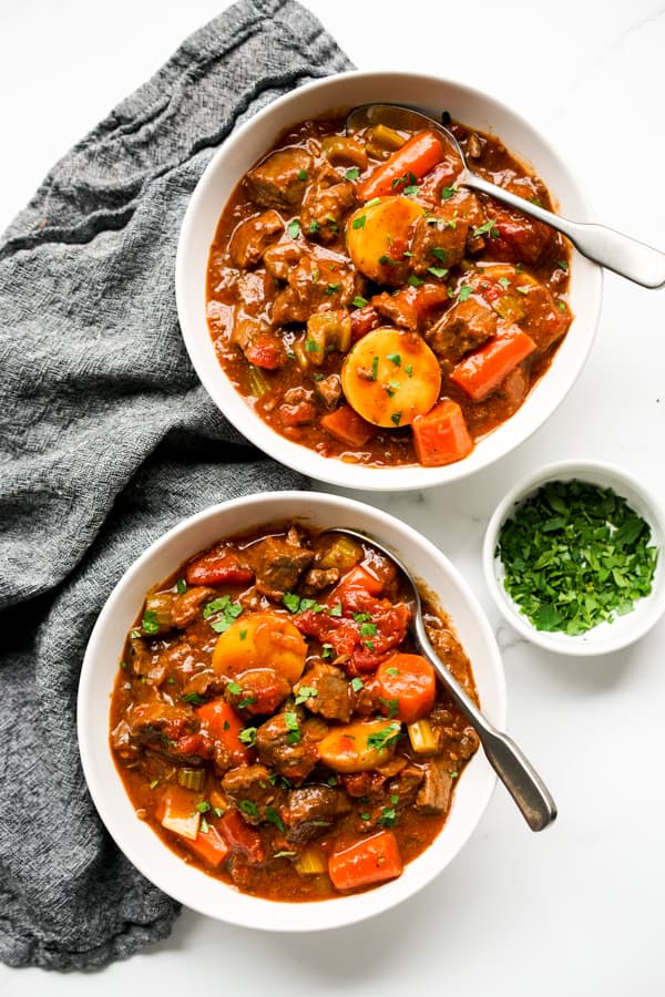 Two bowls of chunky stew filled with beef, carrots, potatoes and tomatoes
