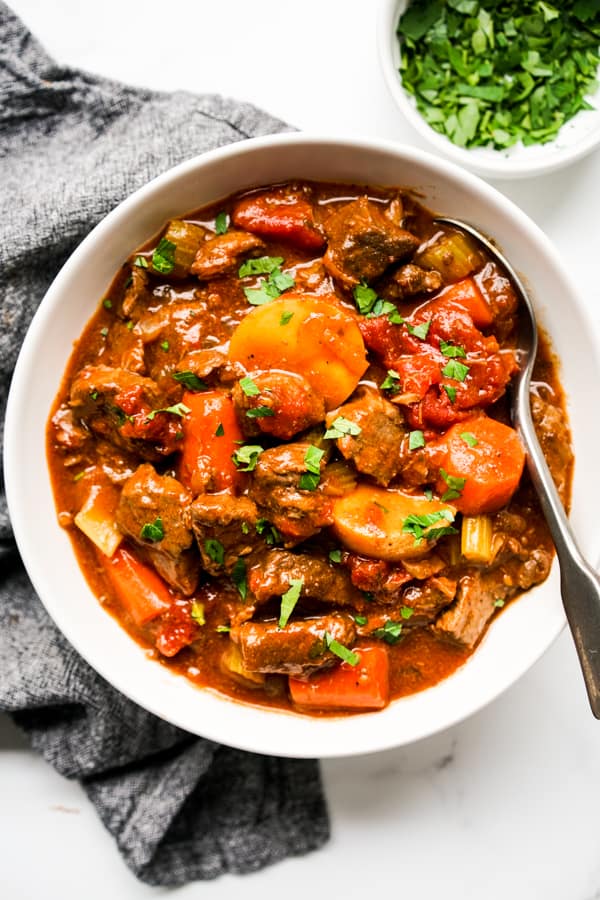 A bowl of hearty chunky beef stew with tomatoes, carrots and potatoes