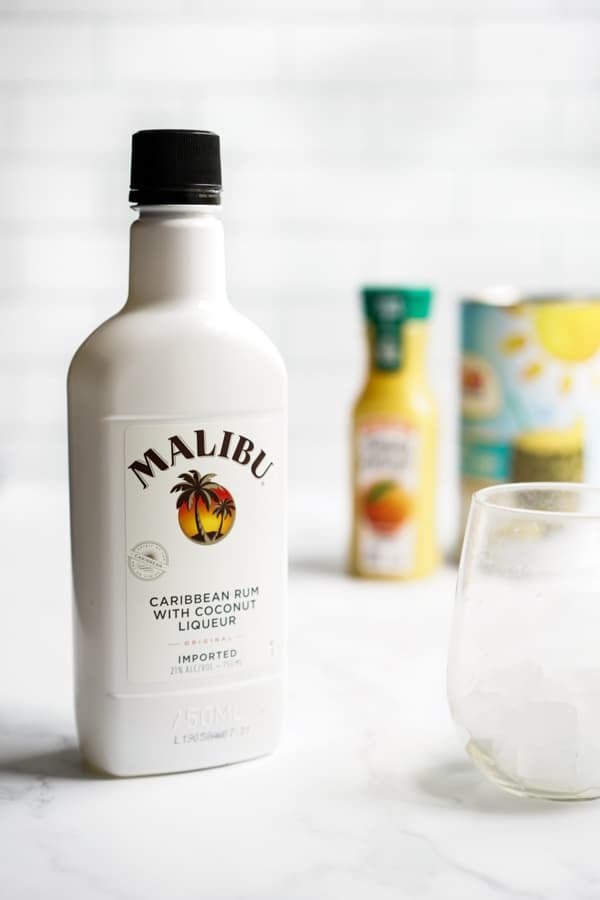 A bottle of Malibu coconut rum with orange juice and pineapple juice in the background