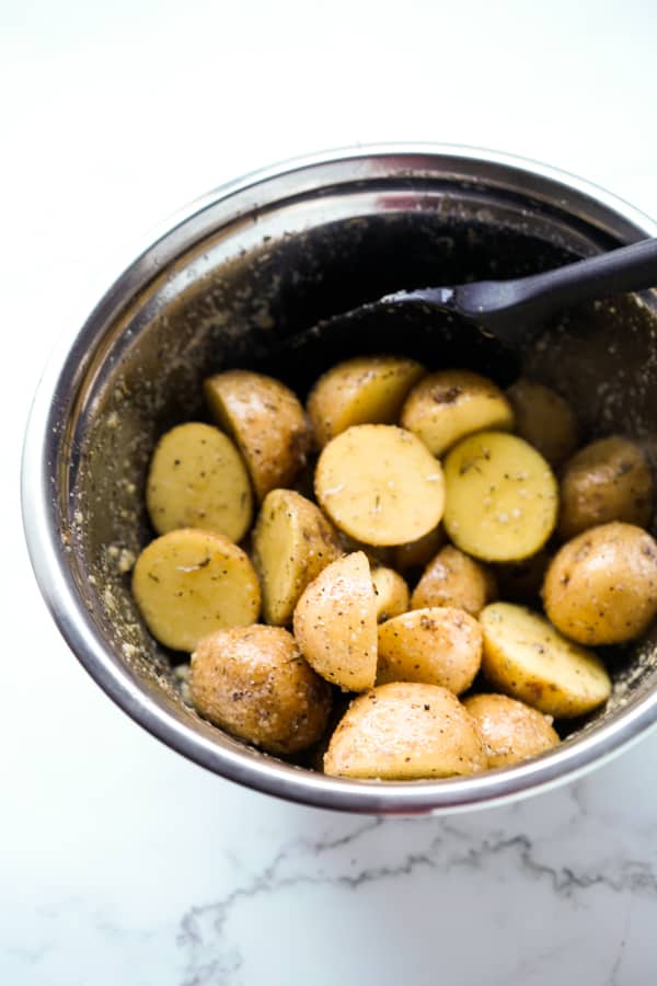 Baby potatoes tossed in oil and seasonings in a bowl