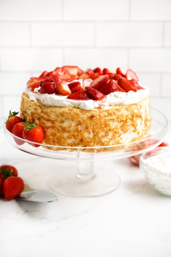 Angel food cake topped with whipped cream and strawberries on a cake stand