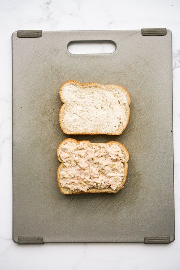 Two slices of bread, one with tuna on top, one spread with butter
