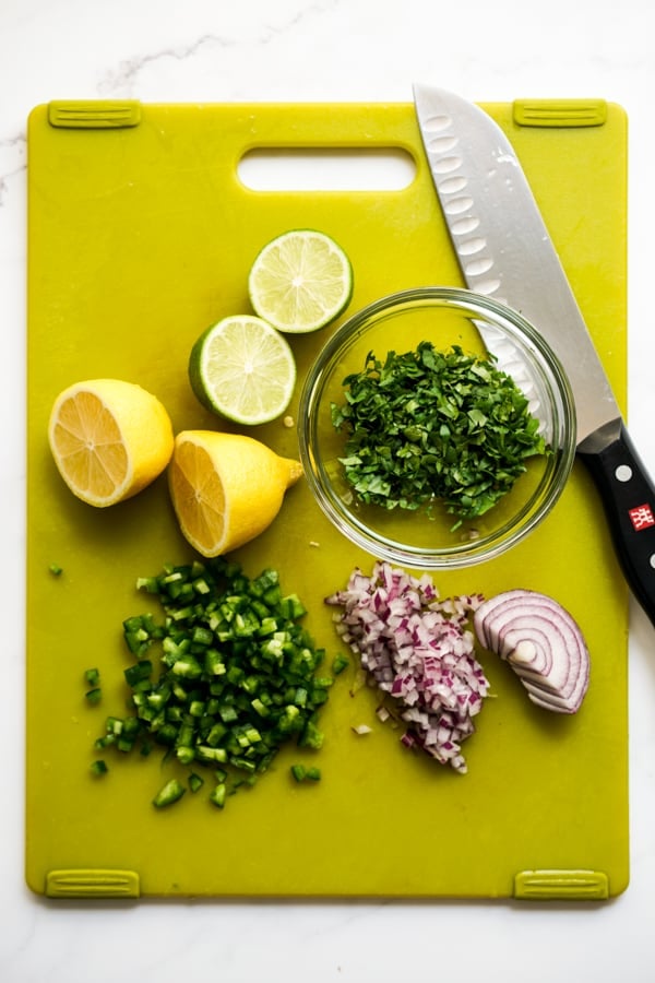 Lemons, limes, cilantro, jalapeño, red onions on a cutting board