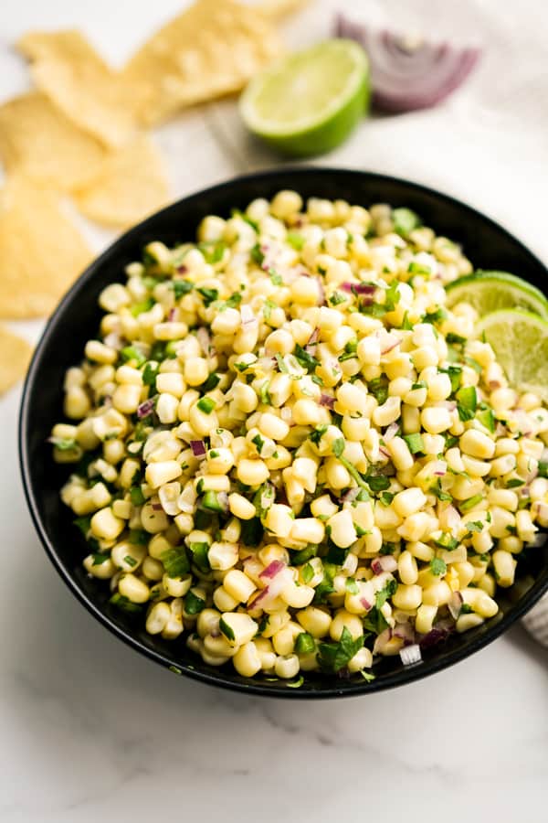 Corn jalapeño salsa in a black bowl, with corn chips in the background