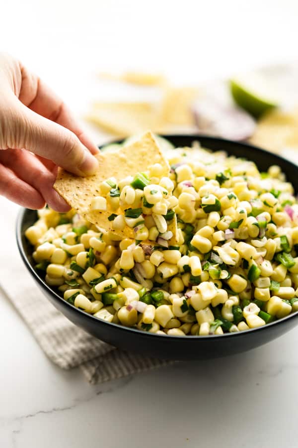 Dipping a corn tortilla chip into a bowl of Chipotle Corn Salsa