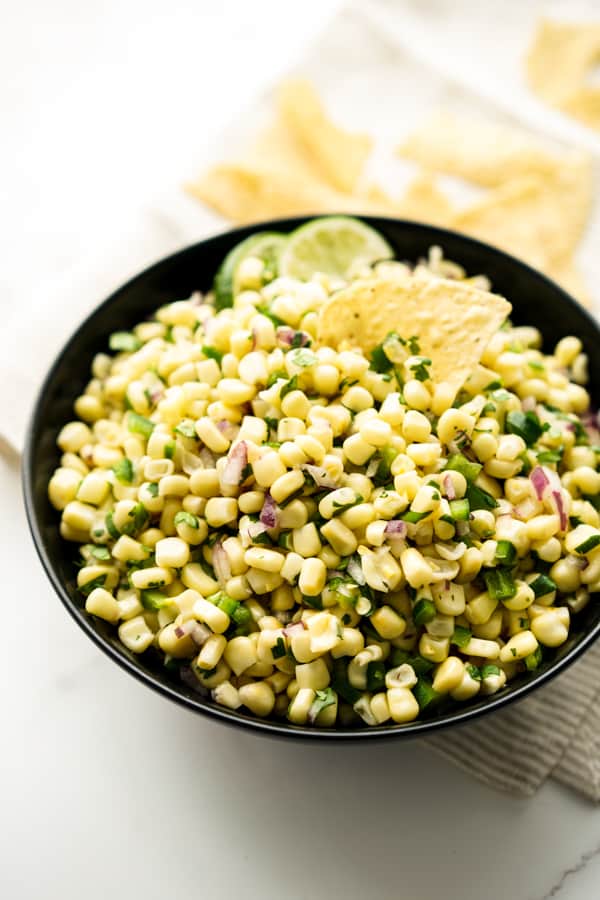 A bowl of Chipotle Corn Salsa with chips and lime wedges on it