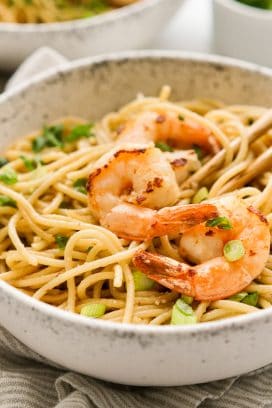 A bowl of garlic noodles with shrimp and green onions, and chopsticks