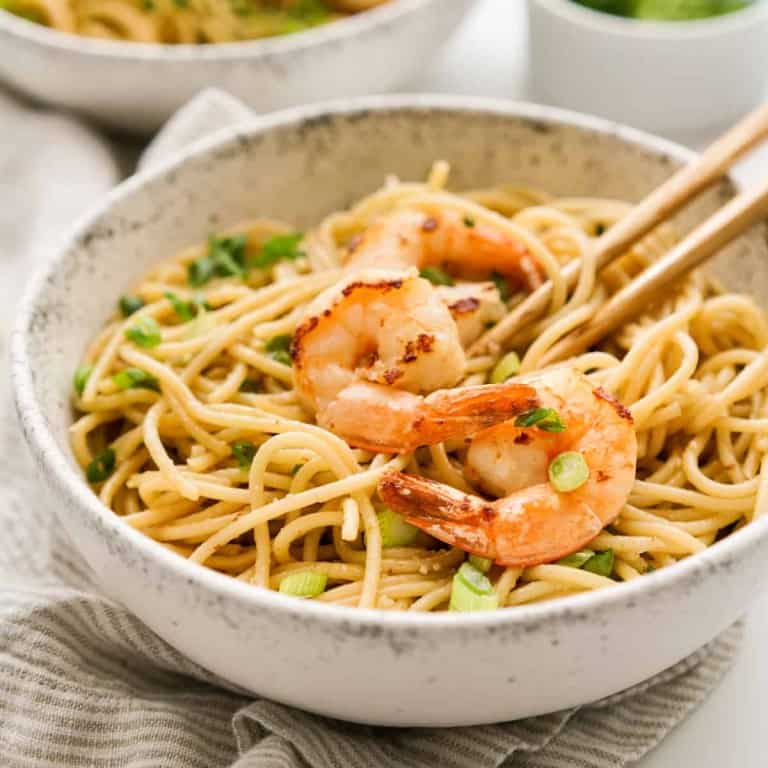A bowl of garlic noodles with shrimp and green onions, and chopsticks